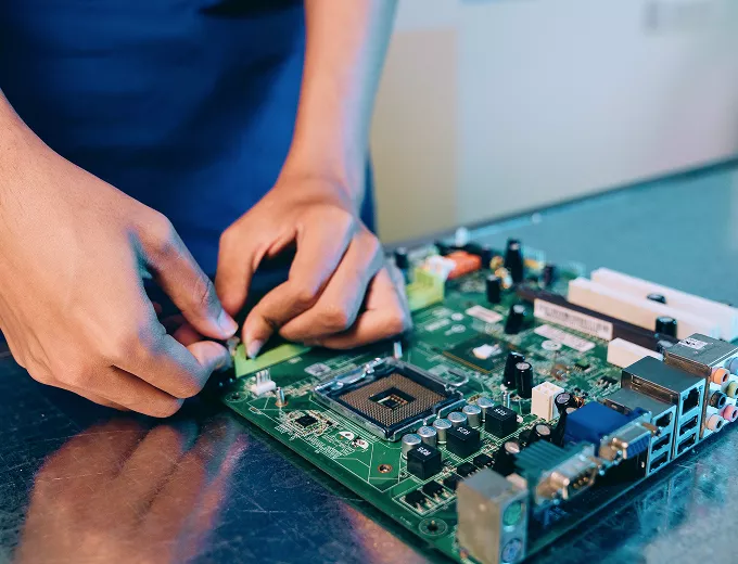 Technician using soldering iron to repair or assemble components on green circuit board motherboard at workbench